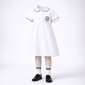 Junior girls DPS-style summer uniform — white tunic with green piping collar, monogram pocket and white socks with green stripes.